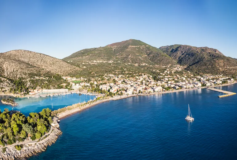Aerial of a coastal town with a sheltered marina and a sailing yacht offshore