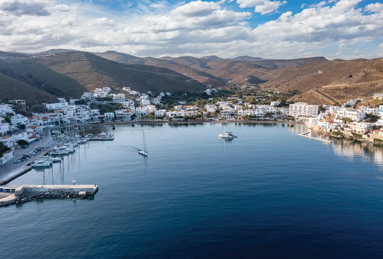 Aerial of a Cyclades island bay town with quay, breakwater and moored sailboats