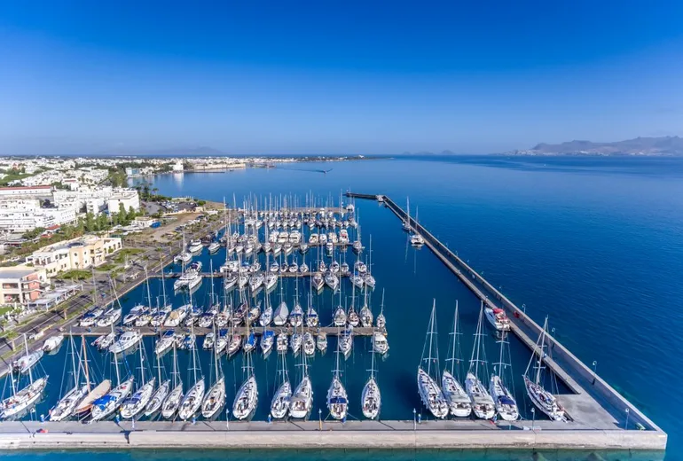 Aerial of a large island marina packed with charter sailboats behind a long breakwater