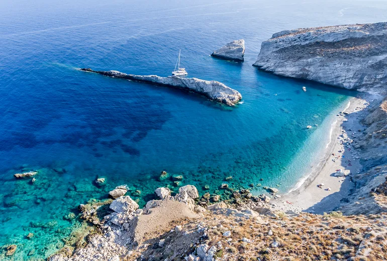 Aerial of a sailing yacht anchored in a rugged white-cliff cove with a pebble beach