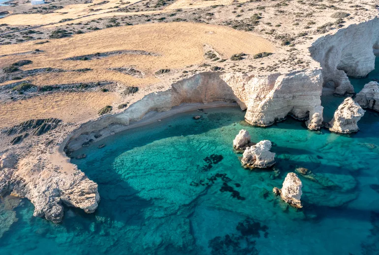 Aerial of a sculpted white rock cove with shallow turquoise water and sea stacks