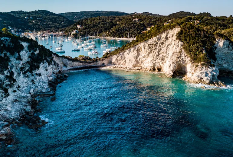 Aerial of white chalk cliffs with the yacht-filled Lakka bay behind on Paxos in the Ionian