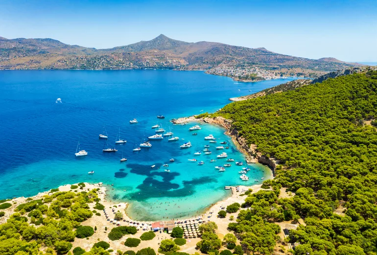 Aerial of yachts moored off a pine-covered islet beach in turquoise water