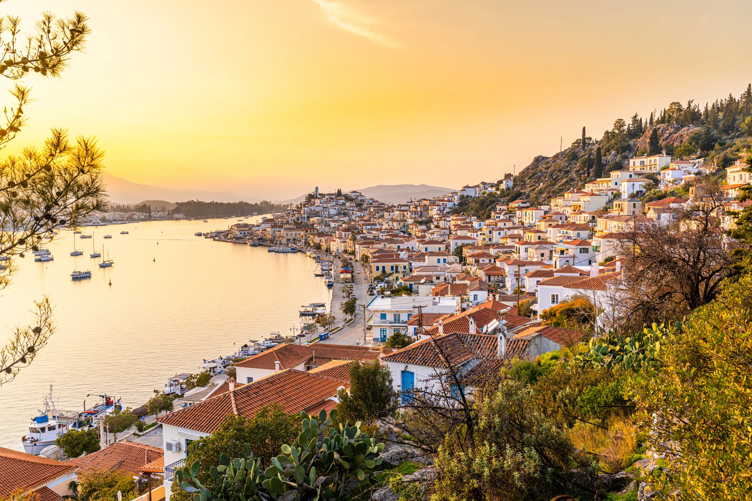 Golden sunset over Poros town rooftops and sailboats at anchor