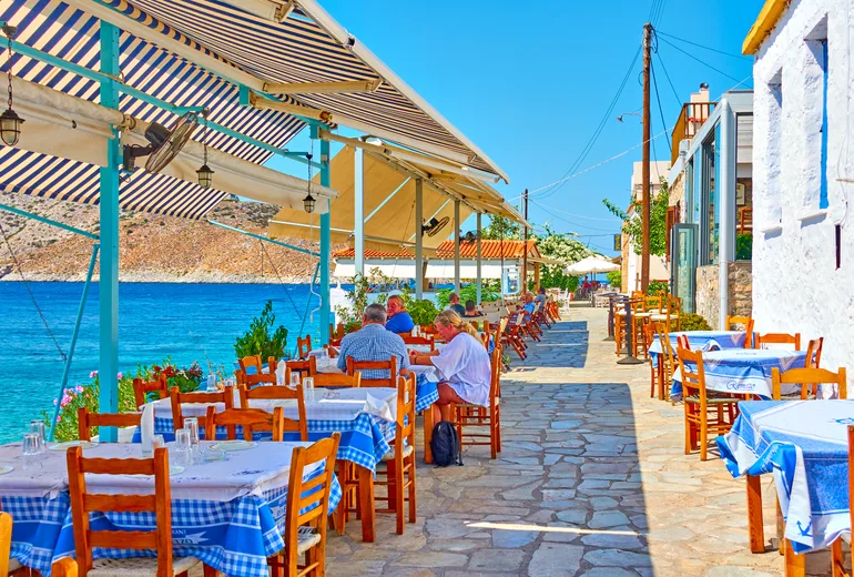 Blue-checked taverna tables along a stone waterfront promenade with a few diners