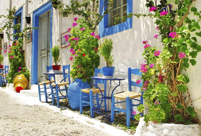 Blue taverna chairs and flowers along a whitewashed Greek island lane