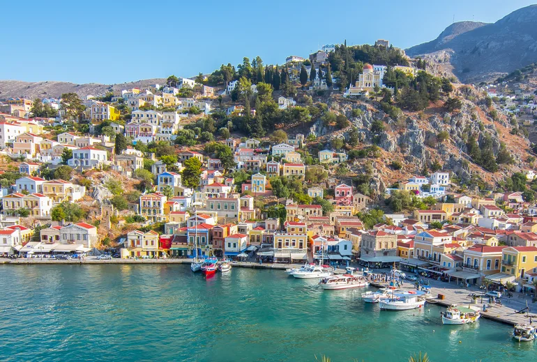 Colourful neoclassical houses rising above Symi island harbour with boats