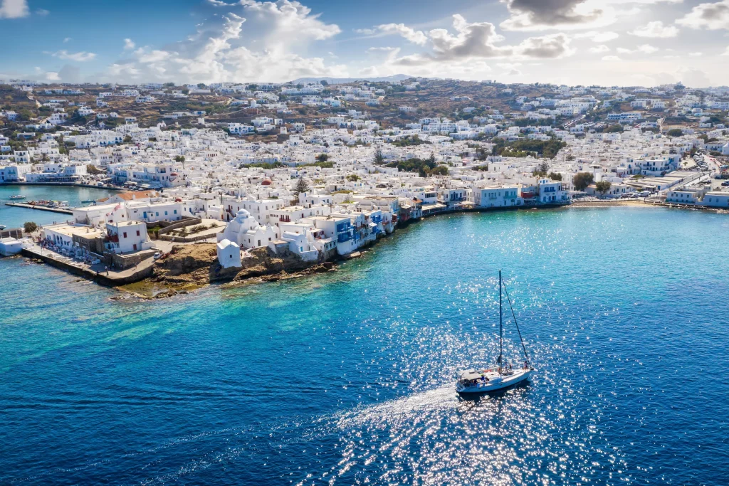 Sailboat motoring toward Mykonos town with whitewashed houses along the waterfront
