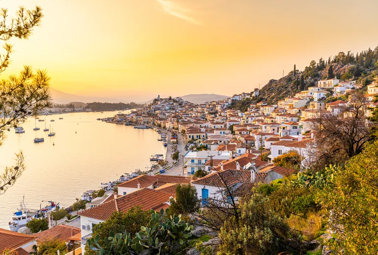 Golden sunset over Poros town rooftops and sailboats at anchor