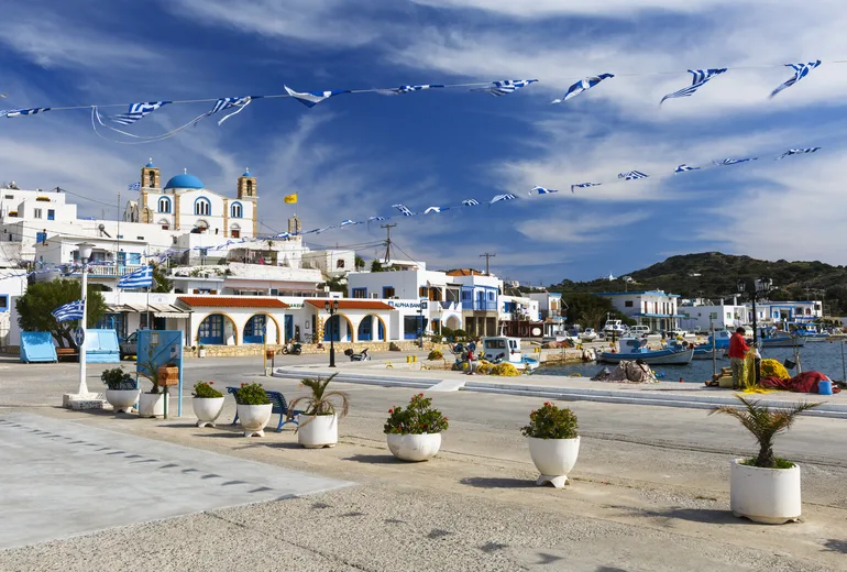 Greek island harbour village with flag bunting, a blue-domed church and fishing boats