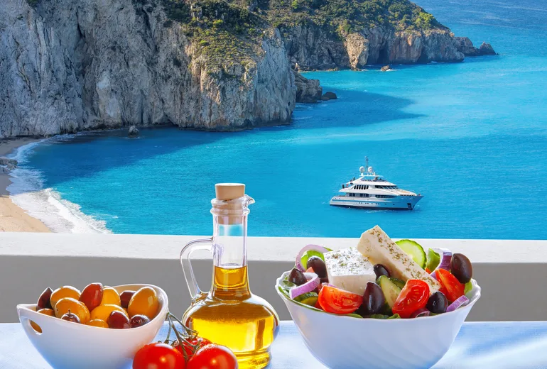 Greek salad, olives and olive oil on a table overlooking a cliff beach