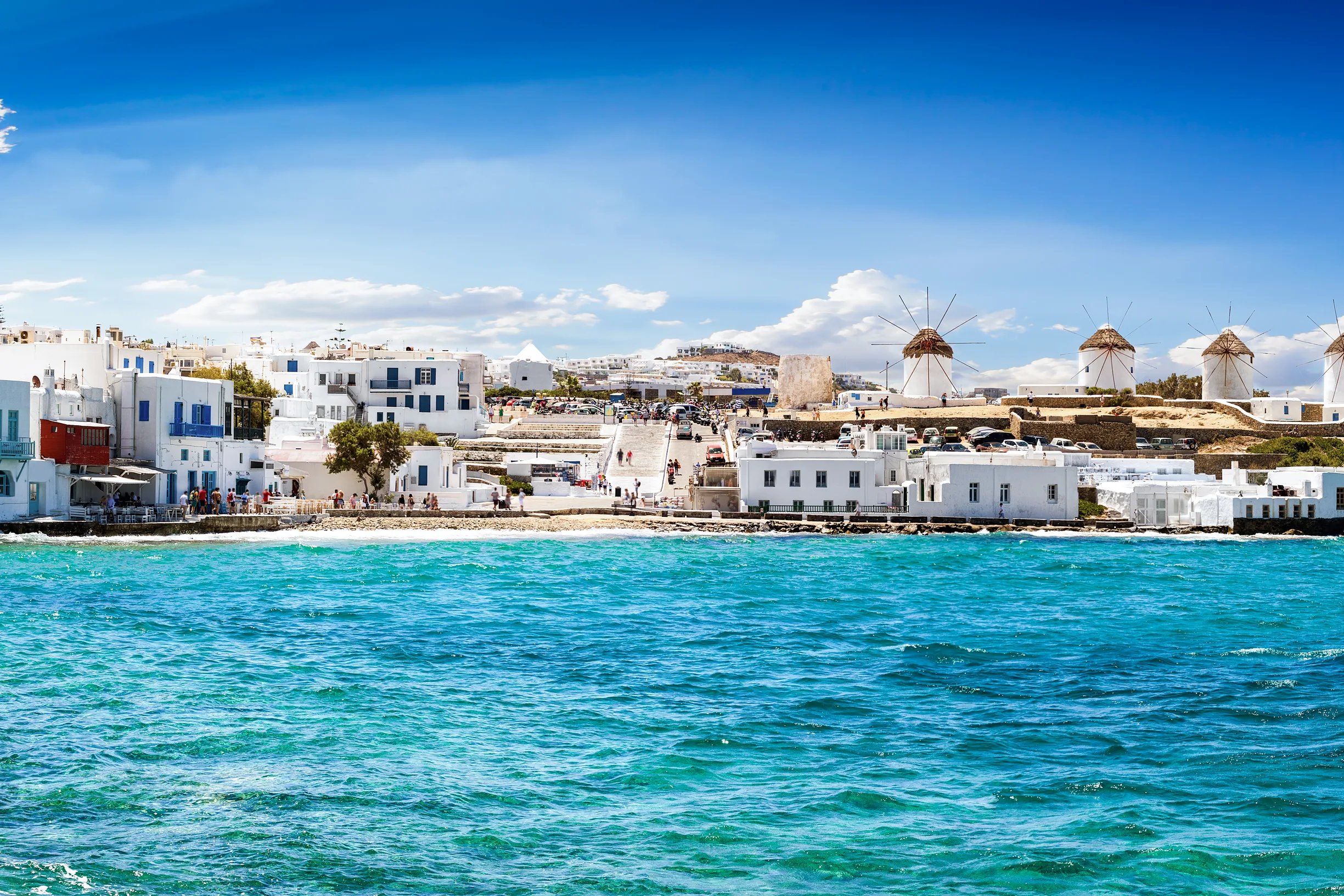 Panorama of Mykonos windmills and waterfront across choppy turquoise sea