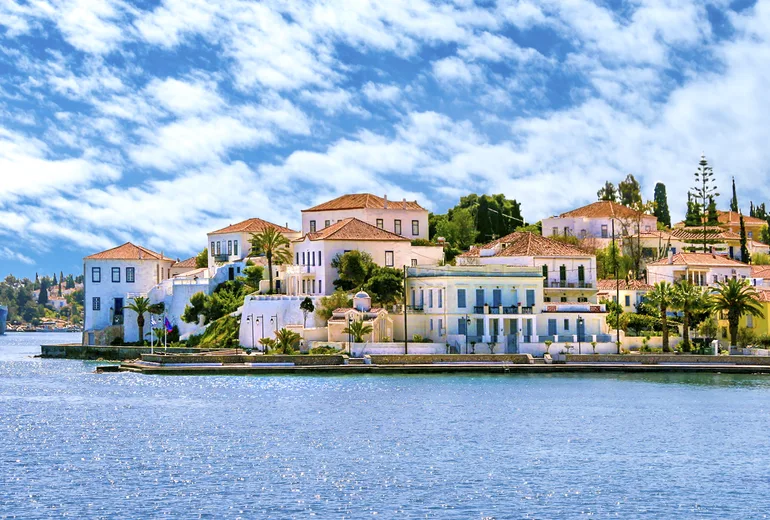 Neoclassical waterfront mansions of Spetses under bright scattered clouds