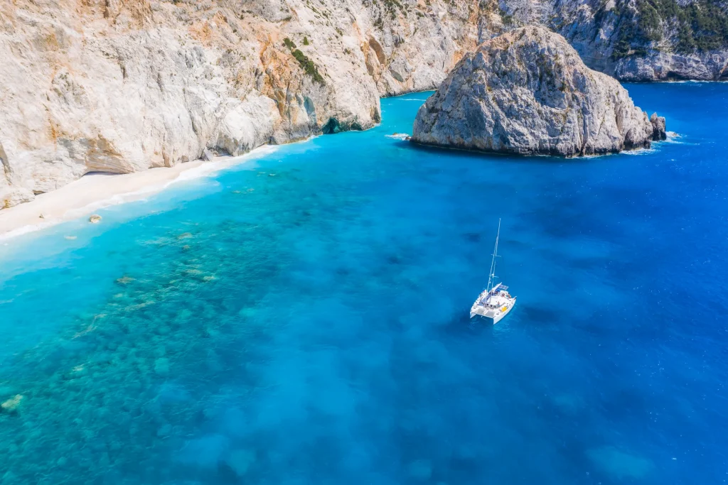Aerial of catamaran anchored beneath white limestone cliffs and beach