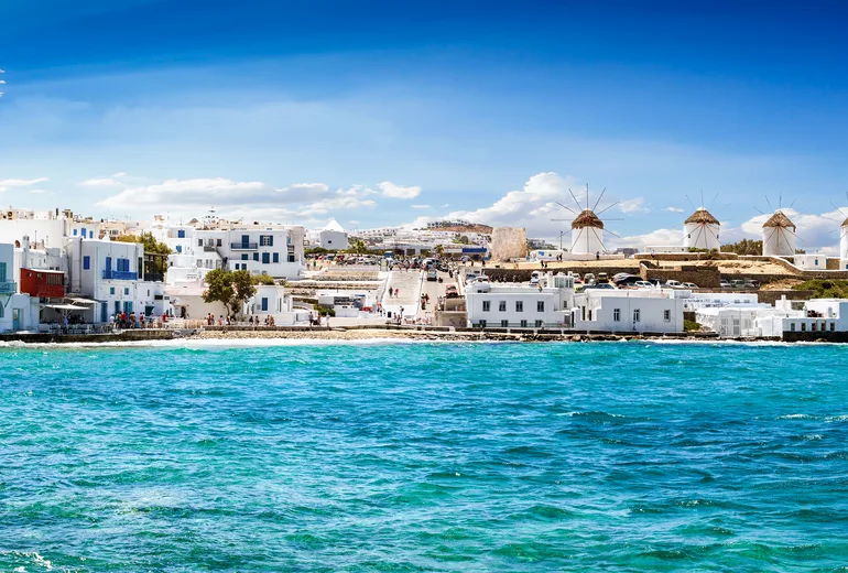 Panorama of Mykonos windmills and waterfront across choppy turquoise sea
