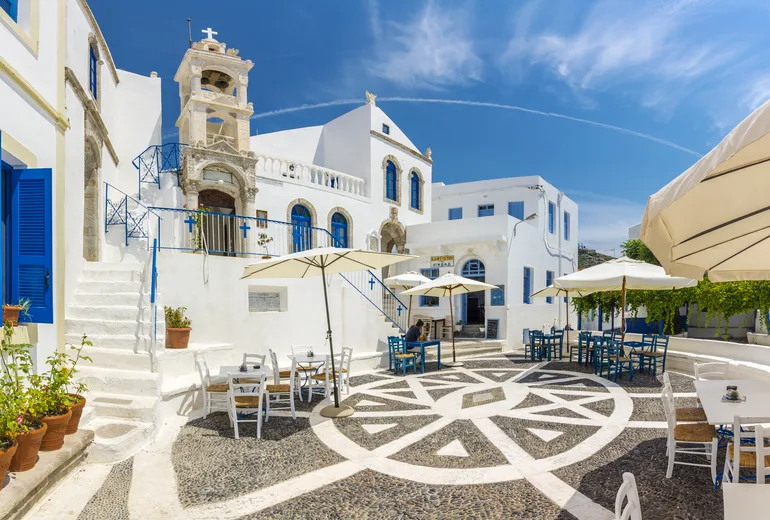 Pebble-mosaic village square with a church bell tower and cafe umbrellas on Nisyros