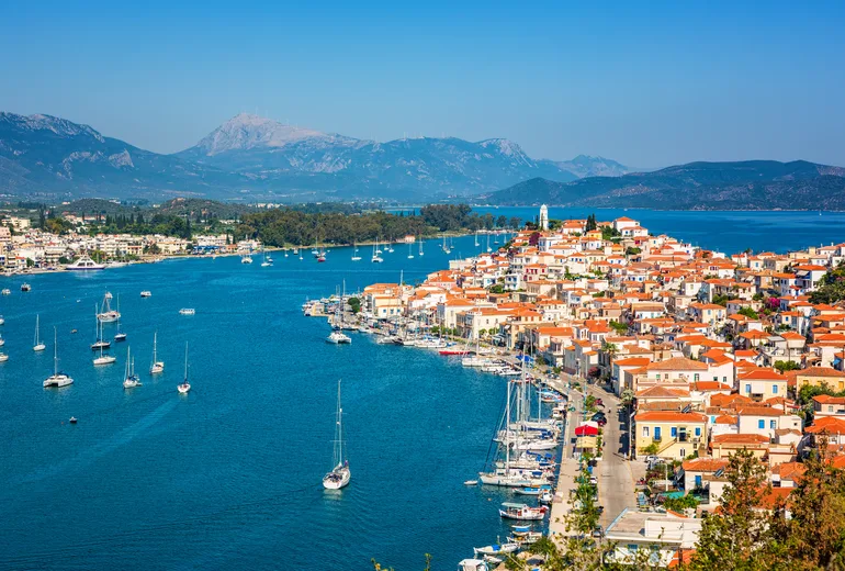 Poros town waterfront with anchored sailboats and a mainland mountain backdrop