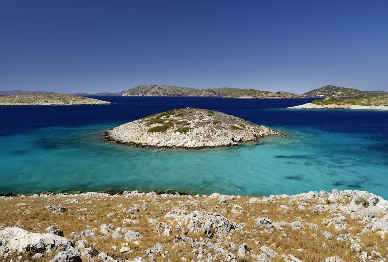 Rocky islet in turquoise shallows among barren Aegean islands