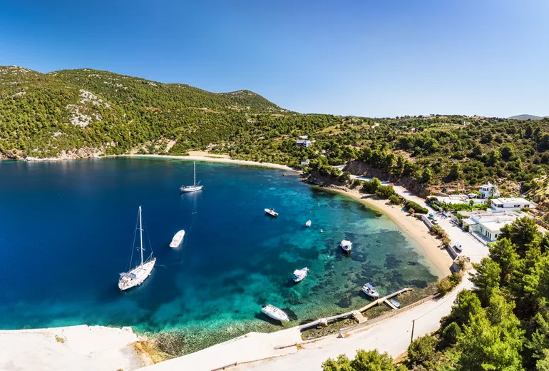 Sailboats moored in a sheltered green bay with a small quay and village houses