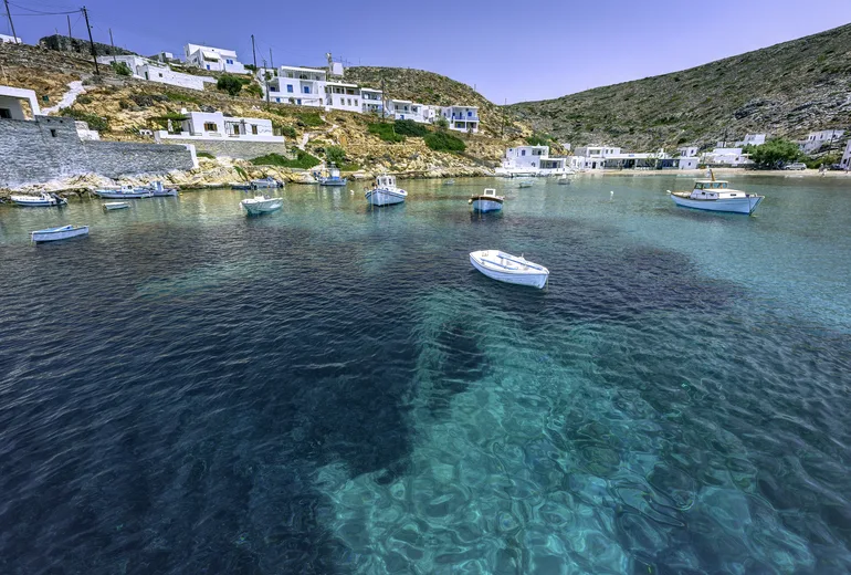Small fishing boats moored in a glass-clear cove below a whitewashed hamlet