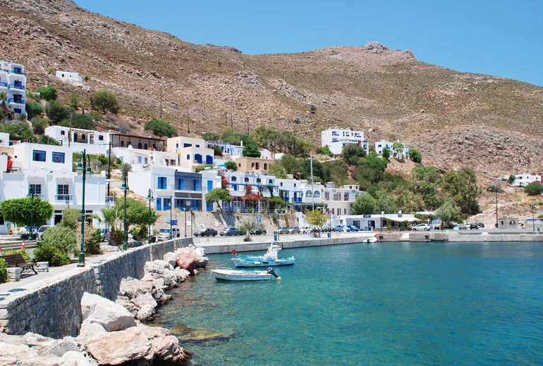 Small Greek island harbour village with fishing boats and barren hills behind