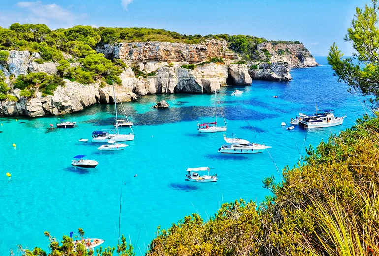 Swimmers and boats in a clear cove beneath limestone cliffs