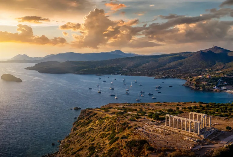 The Temple of Poseidon at Cape Sounion above a sunset yacht anchorage