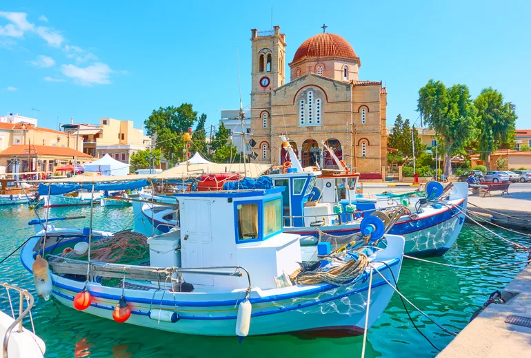 Traditional wooden fishing boats moored before the Aegina harbour church
